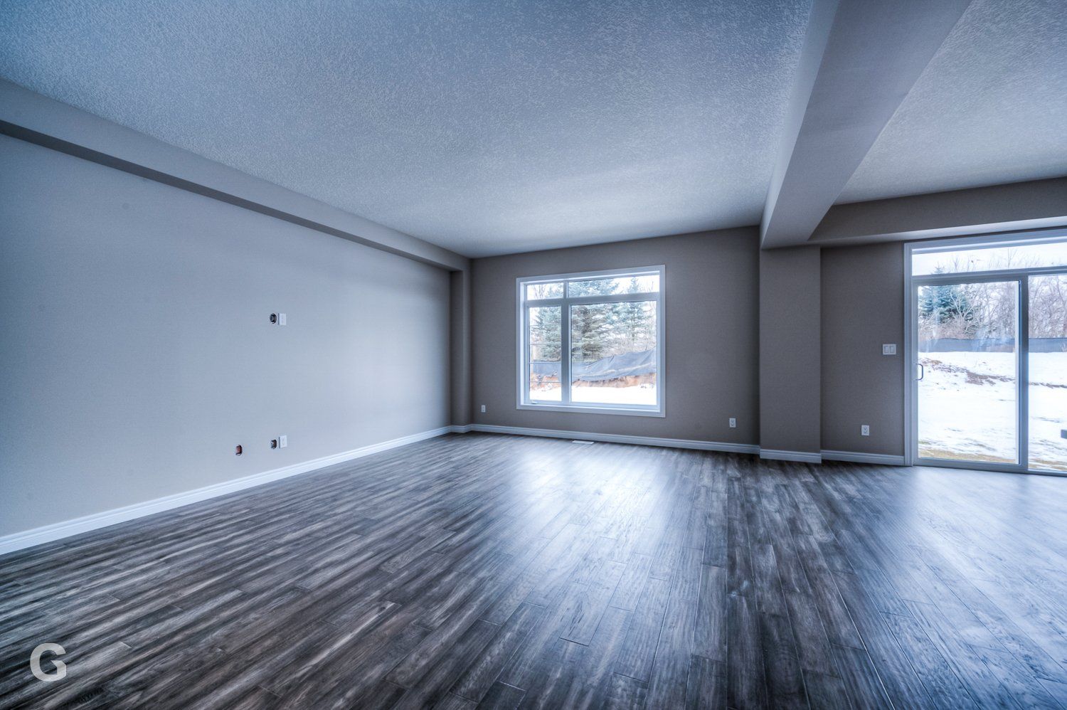 An empty living room with hardwood floors and a large window.