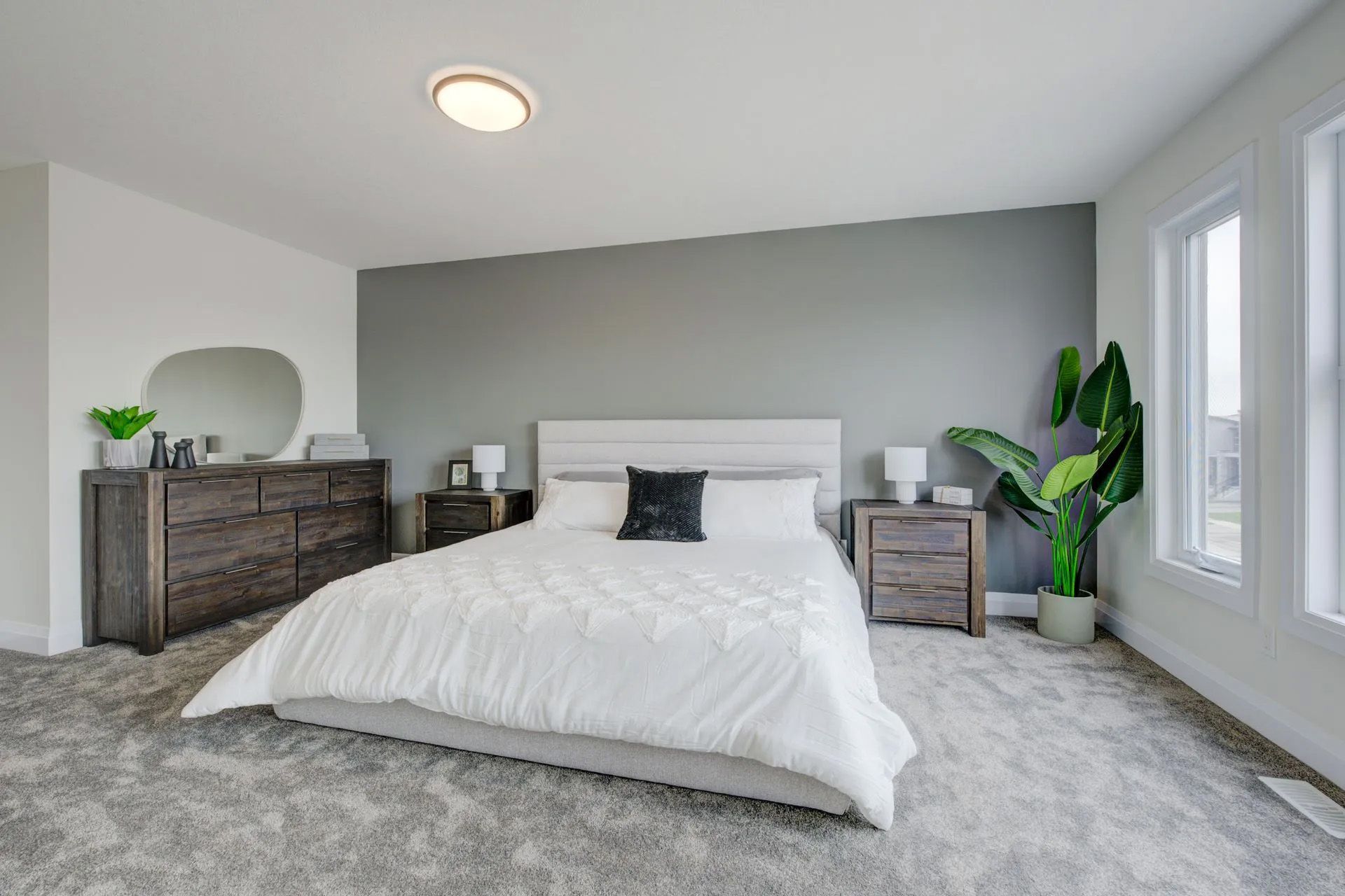 A bedroom with a bed , dresser , nightstand , mirror and plant.