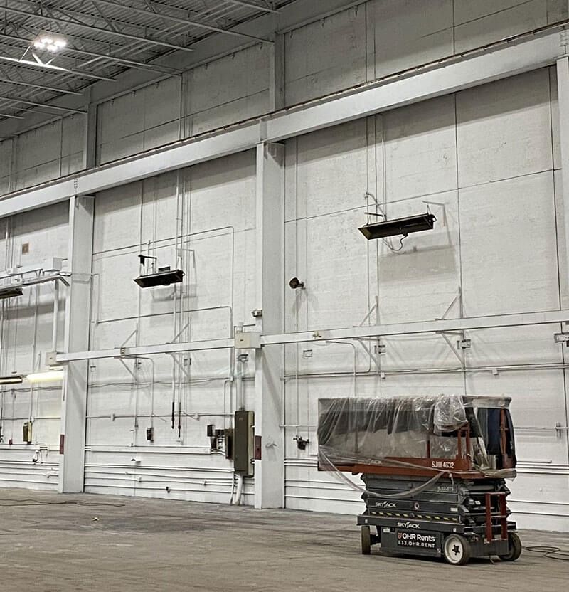 Interior warehouse view with a lift, exposed pipes, and overhead lighting.