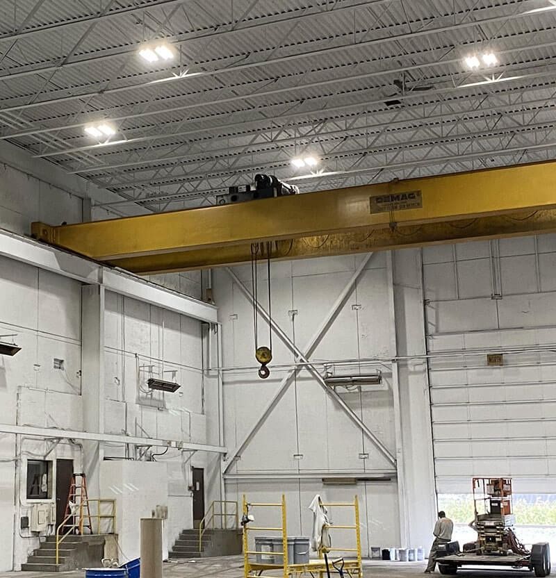 Inside a warehouse with a yellow overhead crane. White walls, ceiling, and metal support beams.