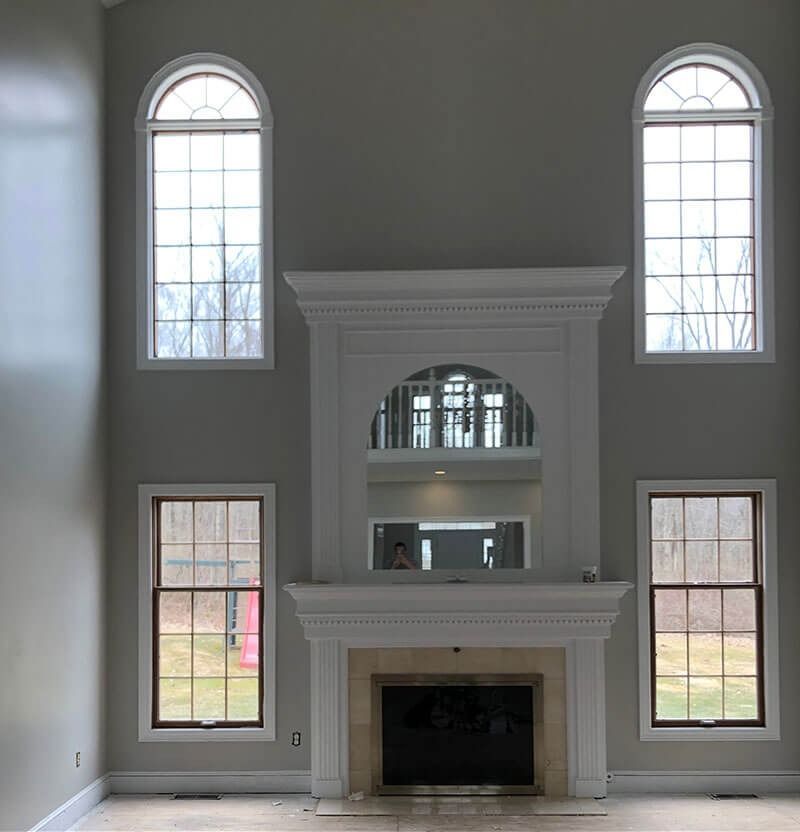 Living room with fireplace, large windows, and high ceilings. Light gray walls and a neutral fireplace surround.