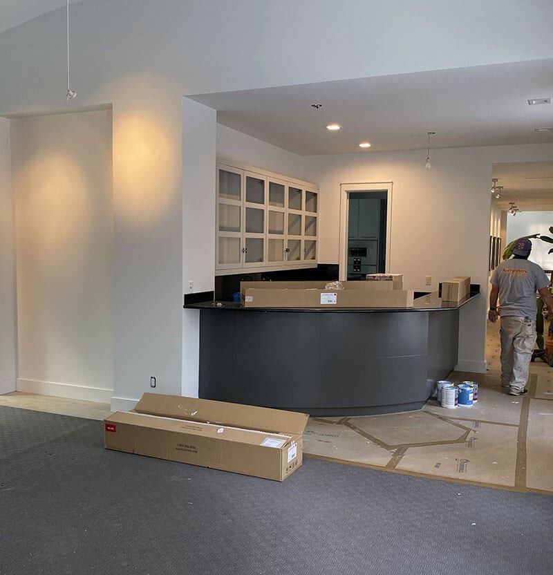 Renovation in progress: Gray cabinets and counter, white walls, a worker walks by.