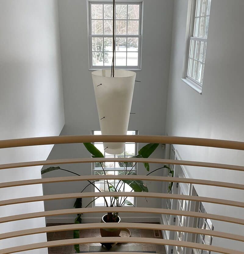 View from above, a staircase with a modern light fixture hanging down, a plant on the landing.