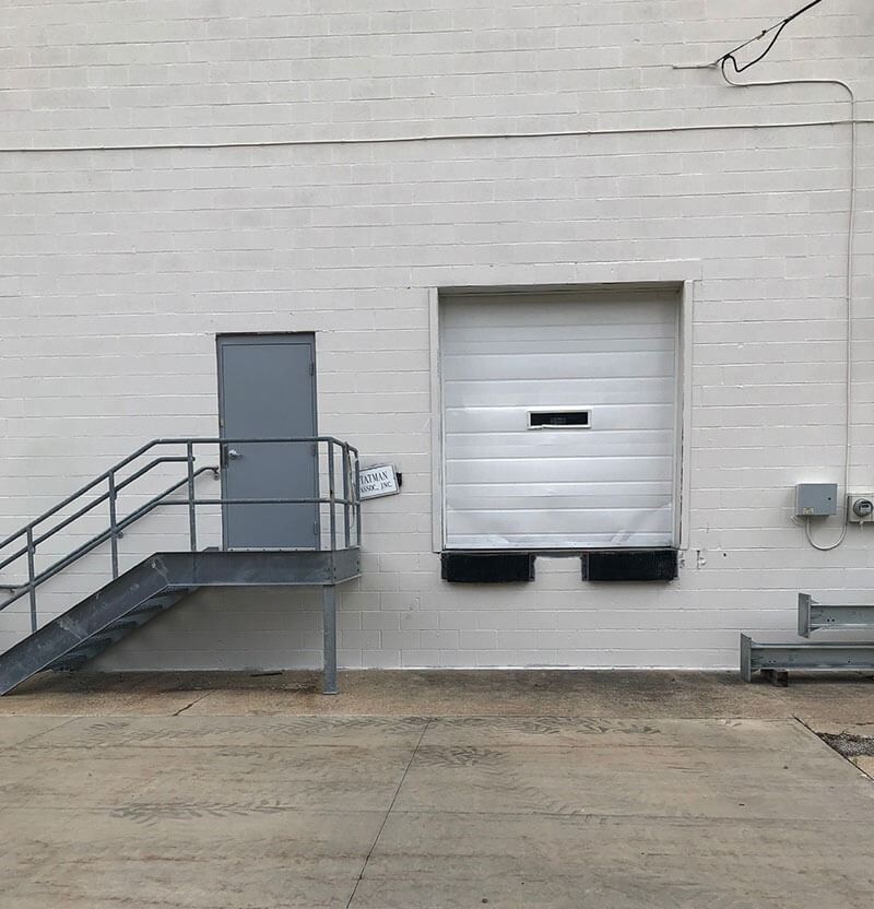 Exterior view: Gray metal stairs and door next to a loading dock door on a white brick building.