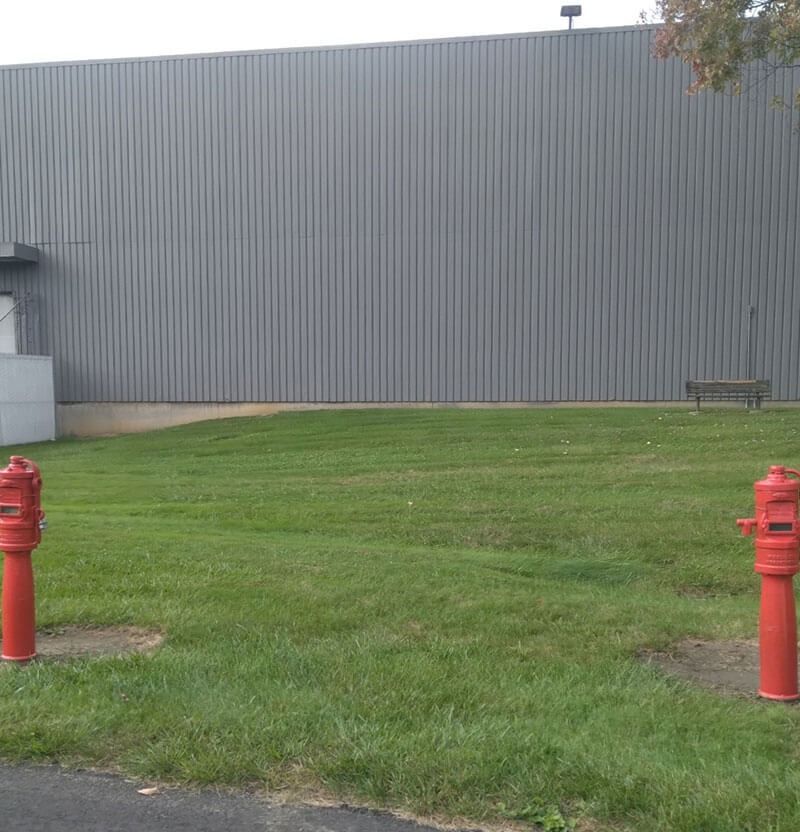 Two red fire hydrants flank a grassy yard in front of a gray industrial building.