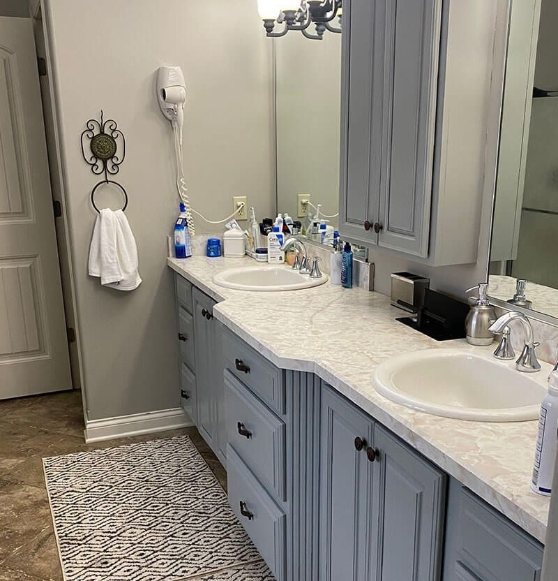 Bathroom with double sinks, blue cabinets, white countertop, and a rug.