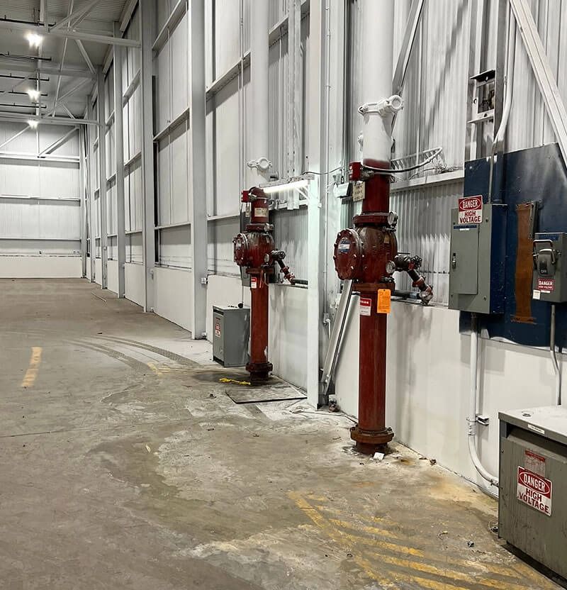 Red fire hydrants line a concrete floor next to electrical boxes in an industrial building.