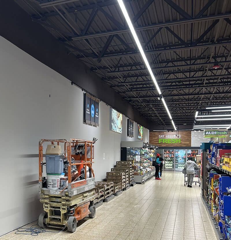 Inside Aldi store, workers near produce section. Construction lift by a white wall.