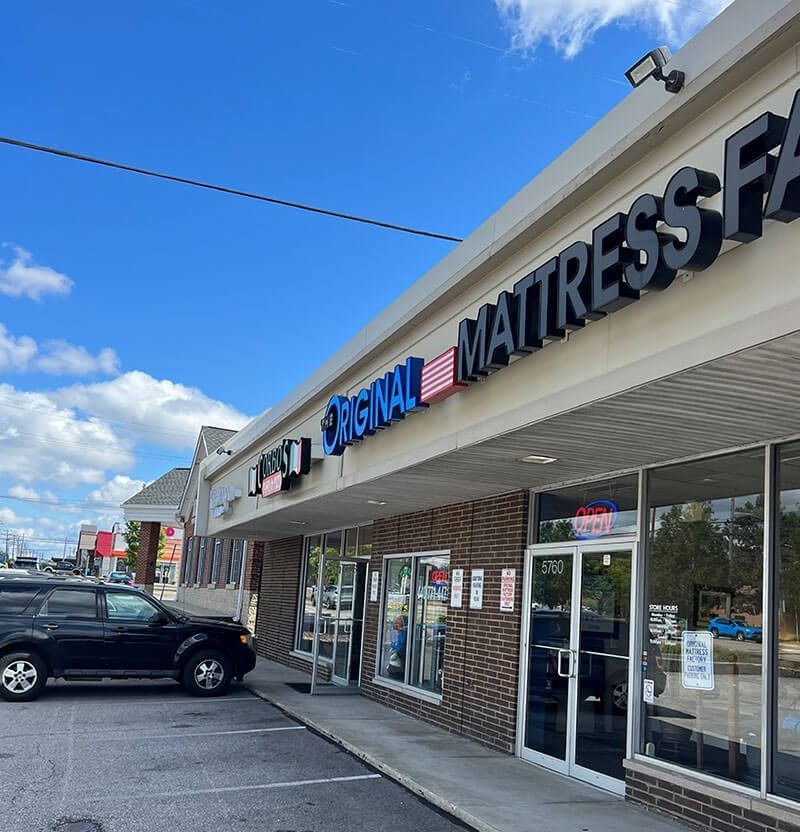 Exterior of Original Mattress Factory store in a strip mall with a black SUV parked in front.