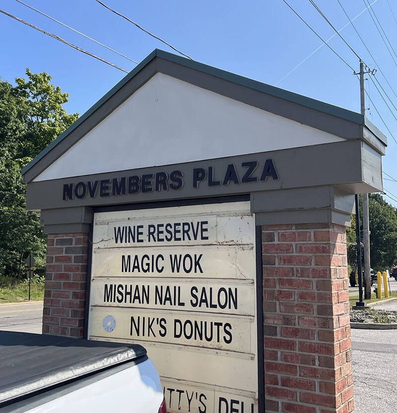 Sign for November's Plaza with listed businesses: Wine Reserve, Magic Wok, Mishan Nail Salon, Nik's Donuts.