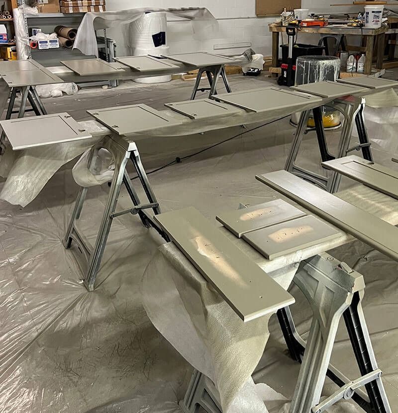 Painted cabinet doors and drawer fronts on sawhorses in a workshop, covered with plastic sheeting.