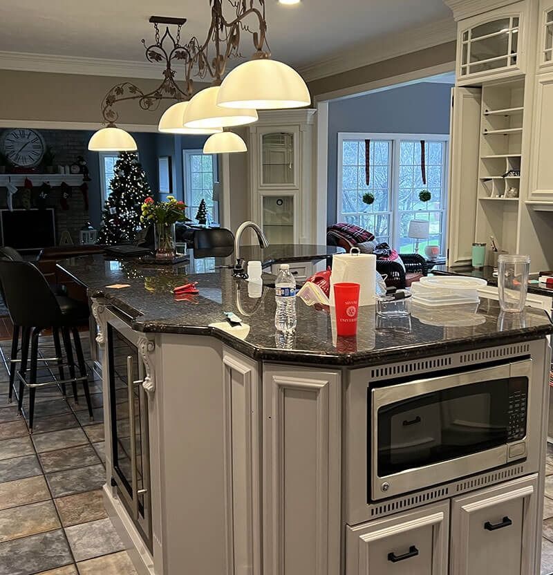 Kitchen with gray island, dark granite countertop, pendant lights, microwave, and wine fridge.