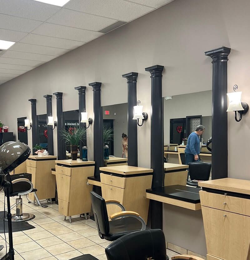 Hair salon with mirrors, black columns, beige cabinets, and customers.