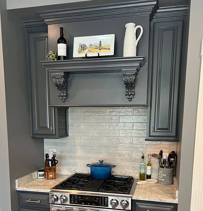 Gray kitchen with stove, backsplash, cabinets, and decorative shelf holding a wine bottle, pitcher, and plate.
