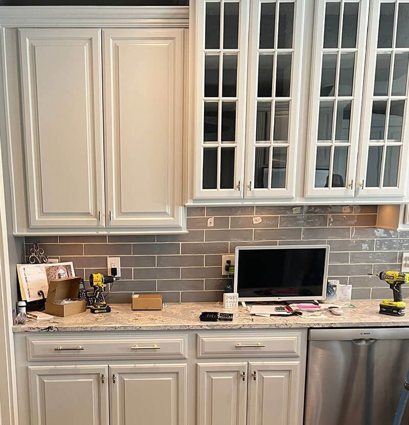 Kitchen cabinets with gray tile backsplash, granite countertop, and appliances. Tools and documents are on the counter.