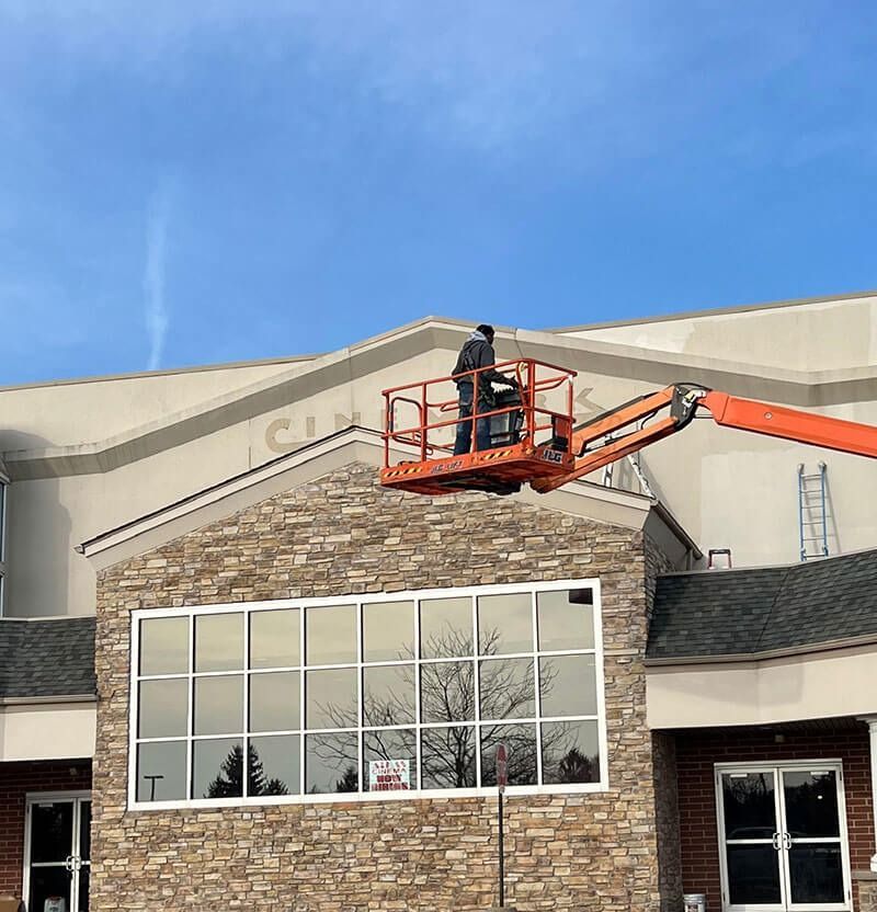 Man on lift working on building facade; clear sky.