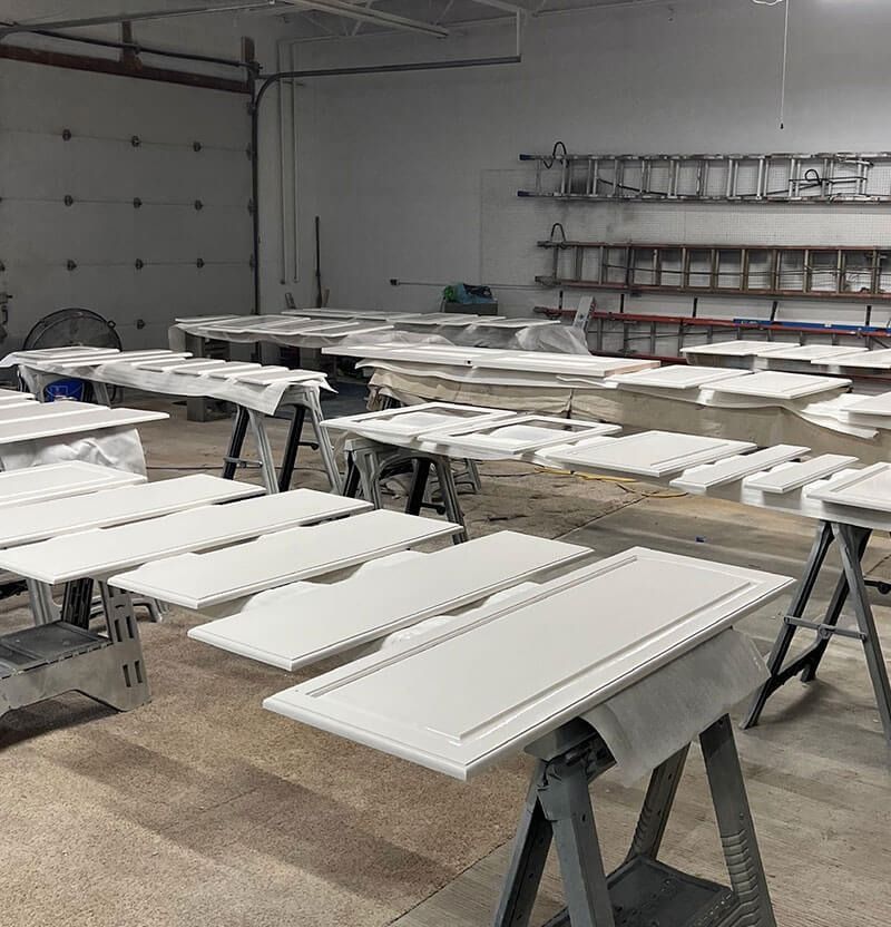 White painted cabinet doors and panels on sawhorses in a workshop, ready to dry.