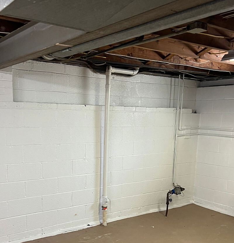 White-painted cinder block basement wall with exposed pipes and ceiling beams.