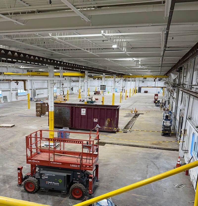 Interior of an industrial space under construction. Red lift in foreground, dumpster, and overhead crane.