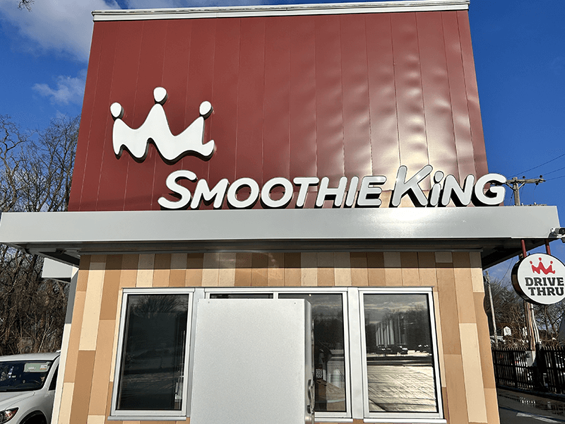 Smoothie King storefront with drive-thru. Red and beige building with logo and sign against a blue sky.