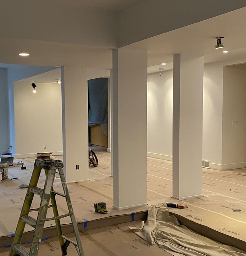Interior room under renovation, featuring white walls, columns, and a ladder.
