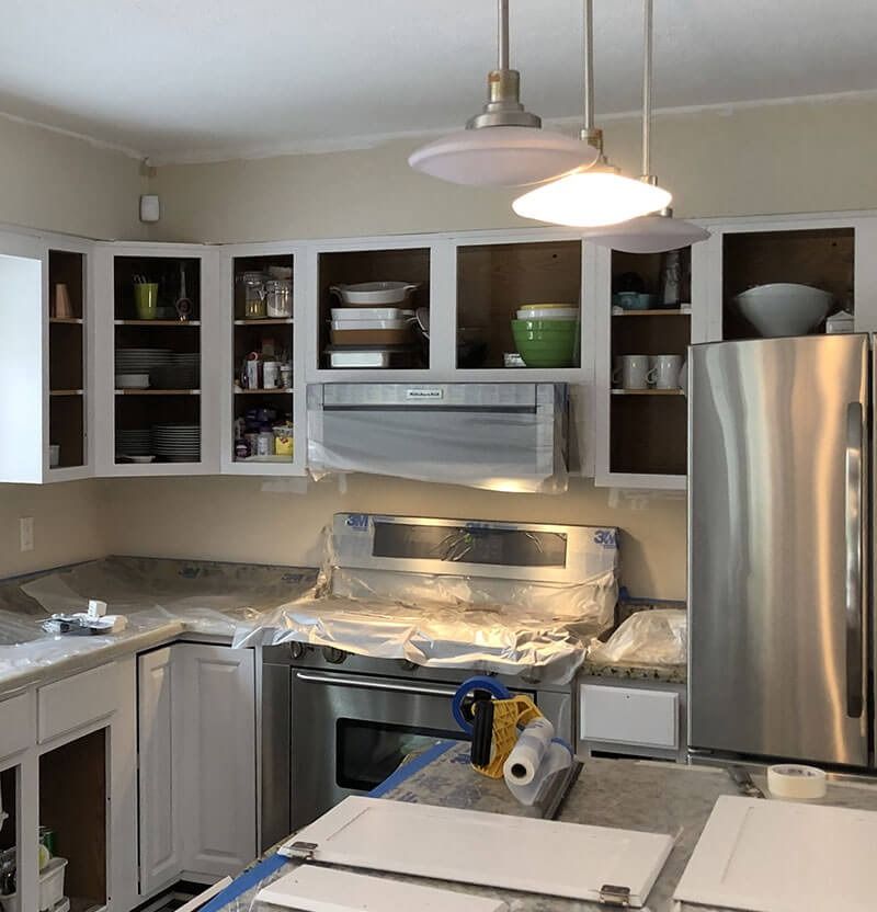 Kitchen during renovation; white cabinets, stainless steel appliances, granite counters, and two pendant lights.