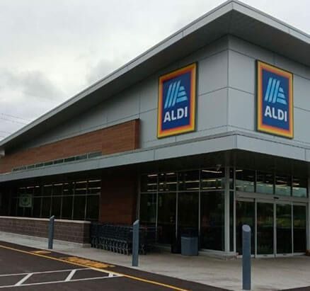 Exterior of an ALDI grocery store with blue and yellow logo. Grey siding and glass windows.