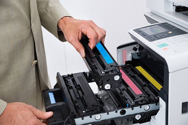 A man is taking a blue cartridge out of a printer.
