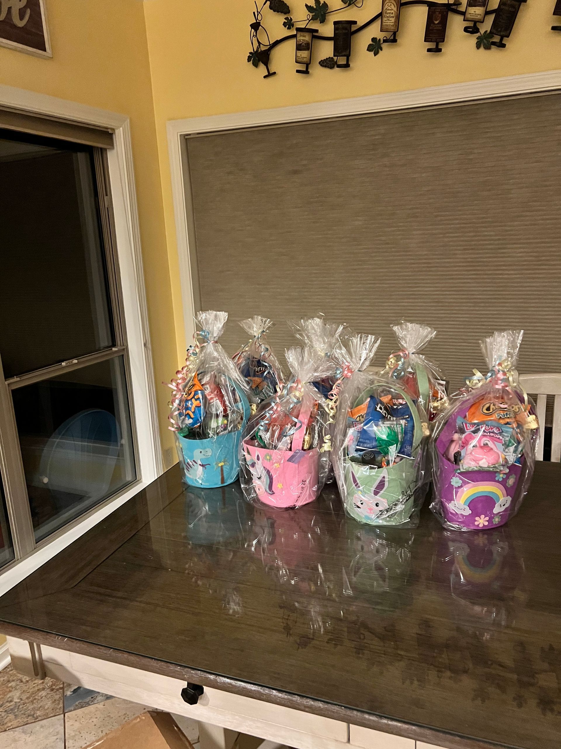 Gift bags with colorful treats lined up on a dark table against a beige wall.