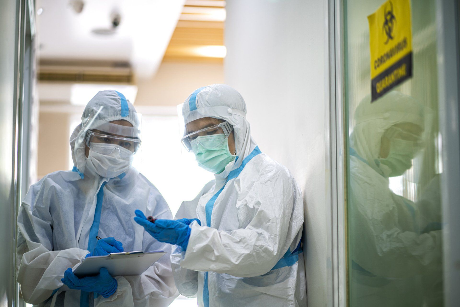 Two scientists in protective suits are looking at a clipboard in a laboratory.