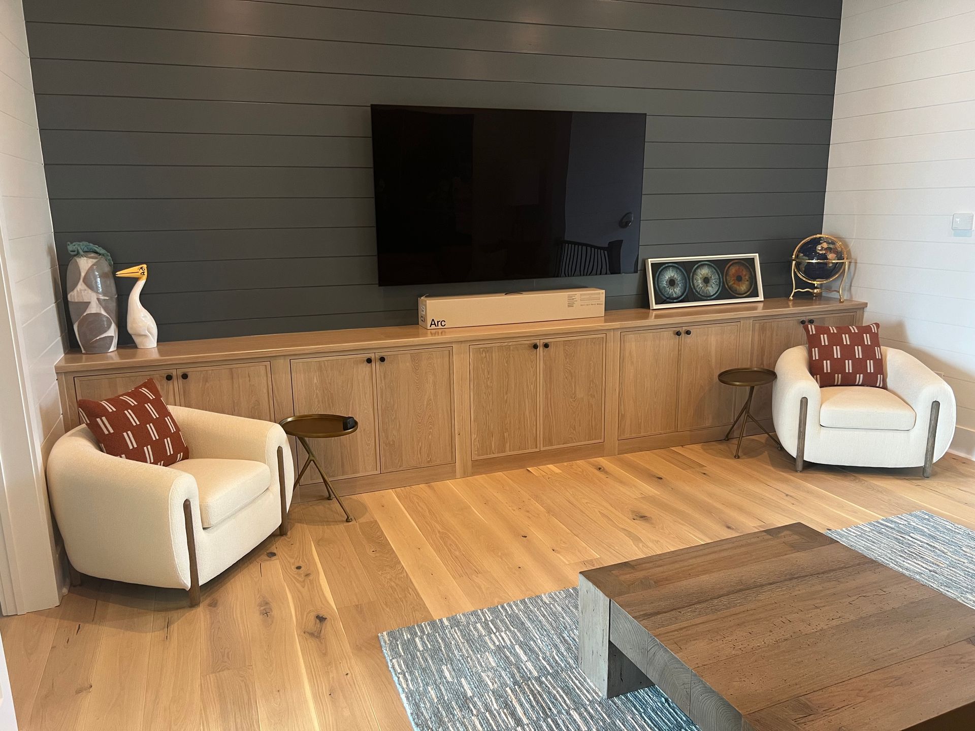 Living room with a large TV above a wooden cabinet, two white chairs, and a coffee table.