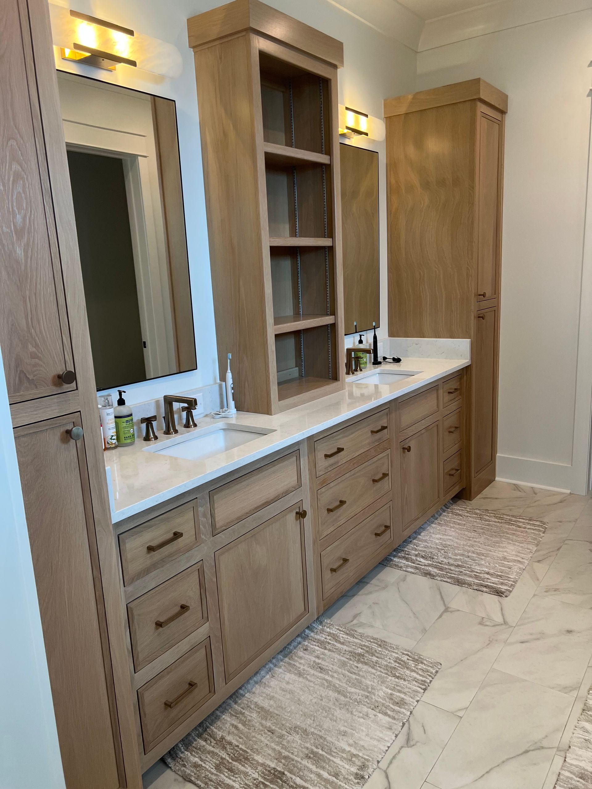 Bathroom with light wood cabinets, white countertops, and marble tile floors.