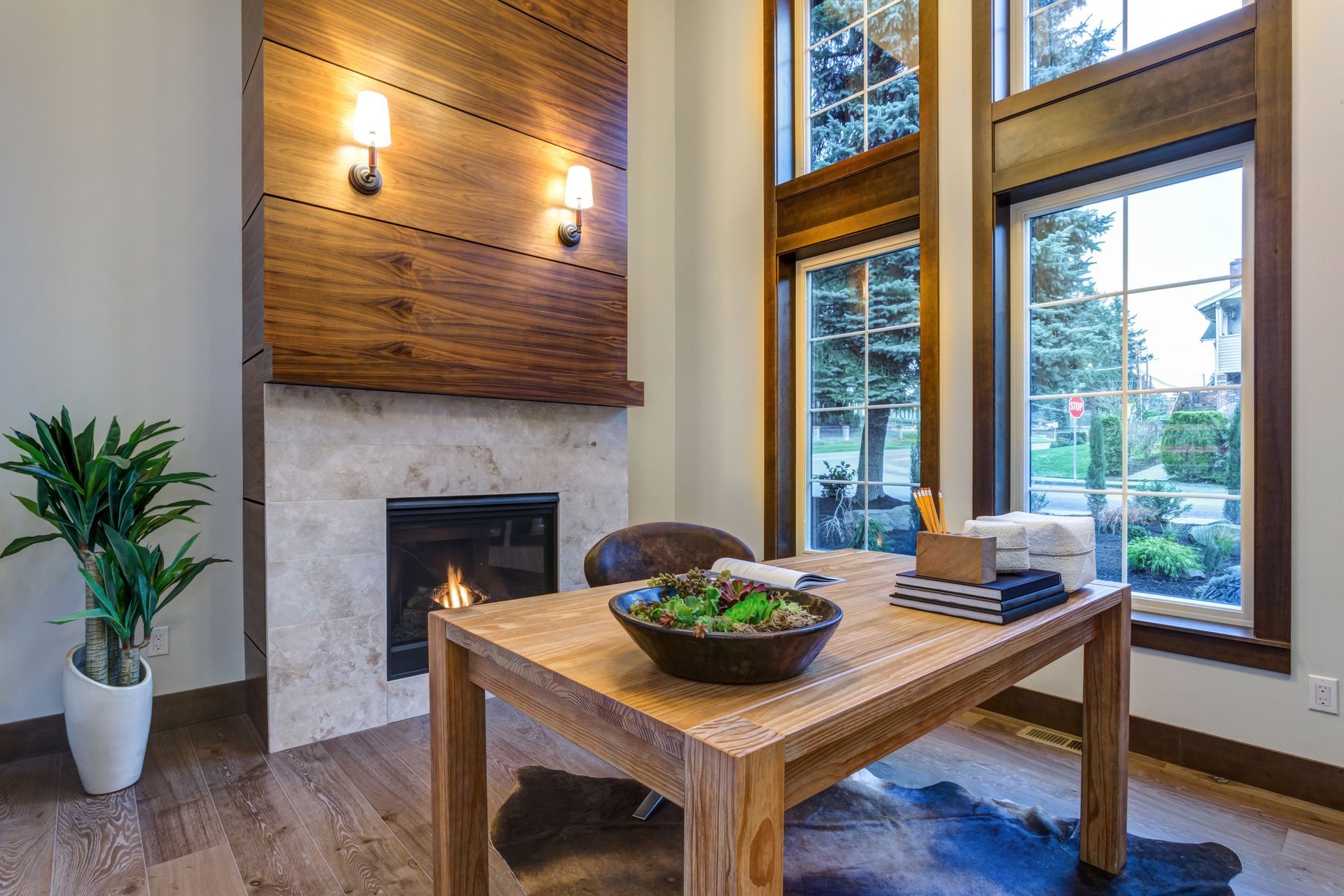 Wooden desk in front of fireplace and windows, featuring a houseplant, art bowl, and leather chair.