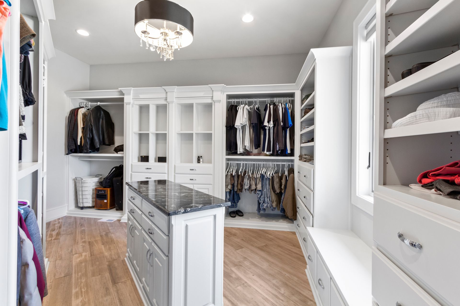 Walk-in closet with white cabinets, center island, wooden floor, clothes hanging.