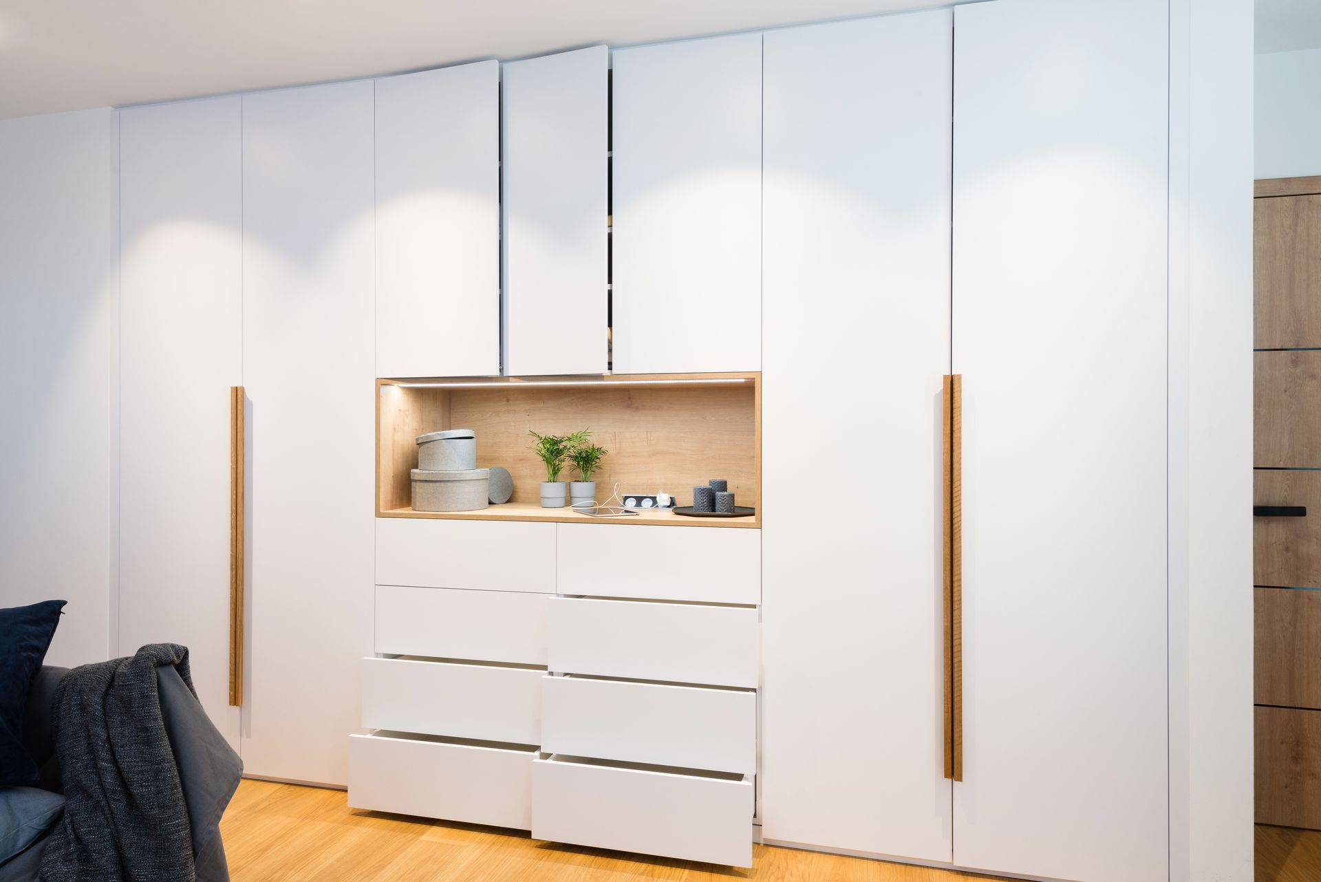 White built-in closet with wooden handles. Central recessed shelf with decor; drawers below.