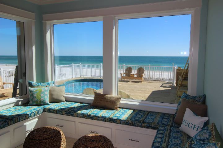 Sunroom with window seating overlooking a beach and pool; blue and turquoise accents.