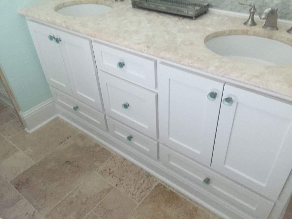 White bathroom vanity with two sinks, marble countertop, and blue knobs.