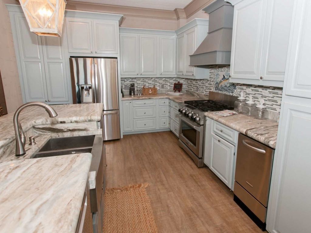 Light blue kitchen with stainless steel appliances, granite countertops, and light wooden flooring.