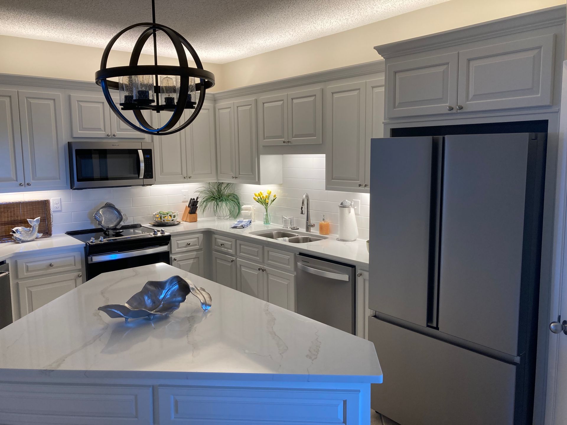 A modern kitchen with light gray cabinets, white countertops, and stainless steel appliances.