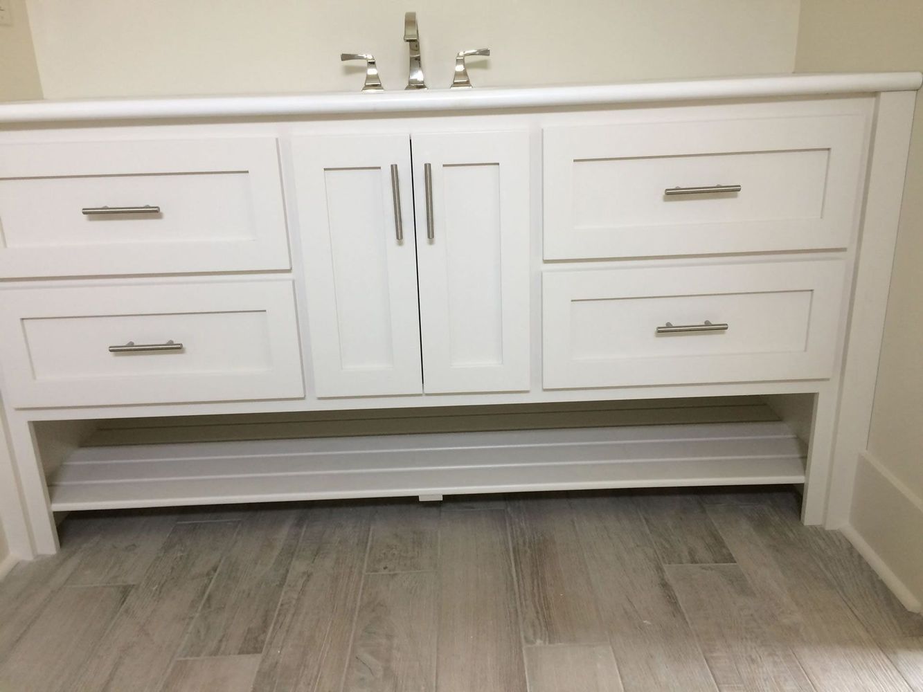 White bathroom vanity with drawers and doors, chrome faucet, and wood-look flooring.
