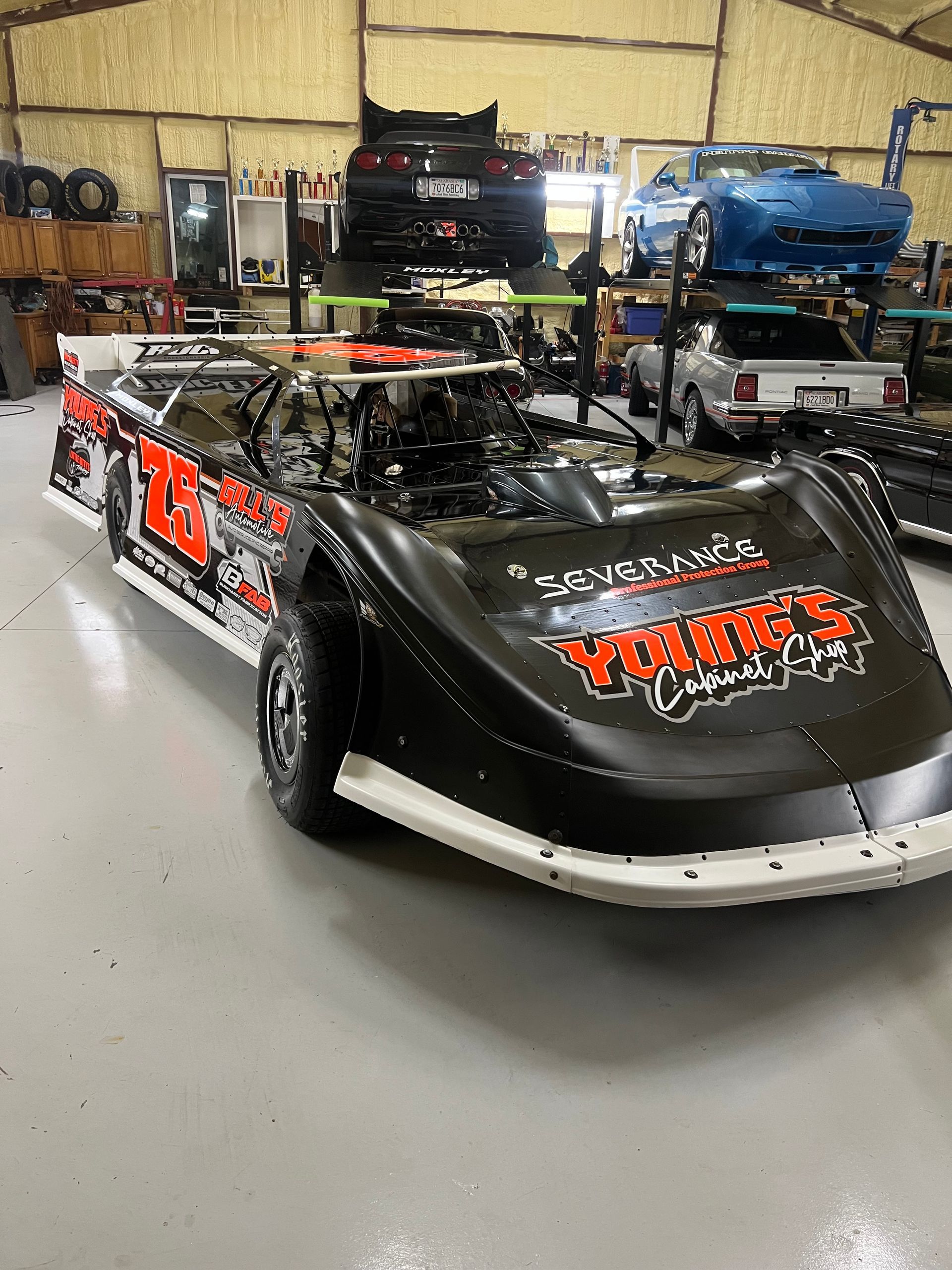 Black and orange race car inside a garage, with other vehicles in the background.