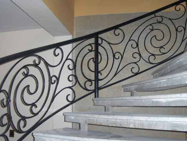 Barandilla de hierro forjado negro con diseño en espiral en escaleras de mármol.