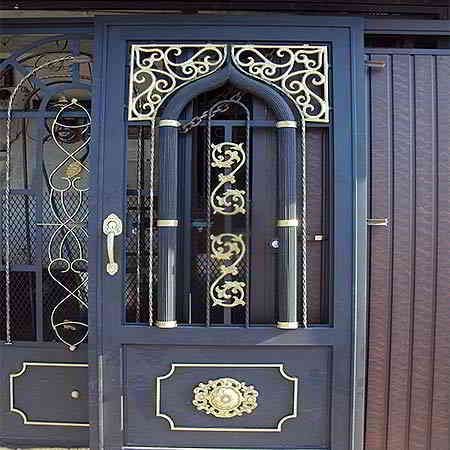 Puerta ornamentada de metal azul oscuro con volutas y detalles dorados.
