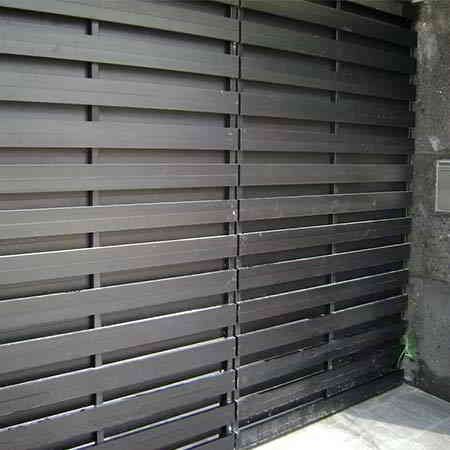 Valla de listones horizontales negros junto a un muro de hormigón.