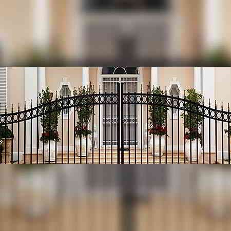 Portón de hierro forjado negro frente a una casa de color claro con macetas a ambos lados.