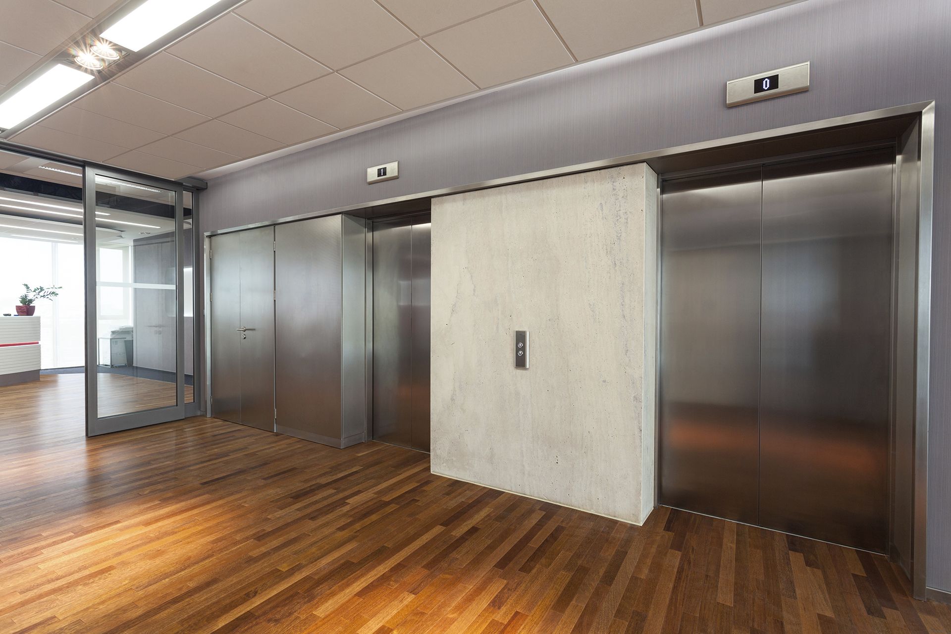 Dos ascensores en un edificio moderno con suelo de madera y pared de cristal.