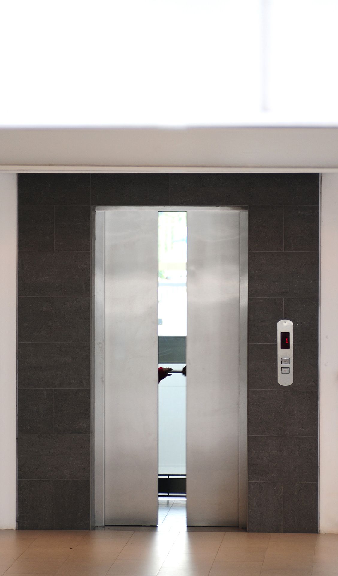 Ascensor con puertas de acero inoxidable abiertas en el vestíbulo de un edificio. Pared de azulejos oscuros. Panel de control del ascensor.