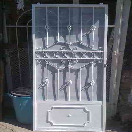 Puerta de seguridad de metal blanco con motivos decorativos en espiral y mosquitera.