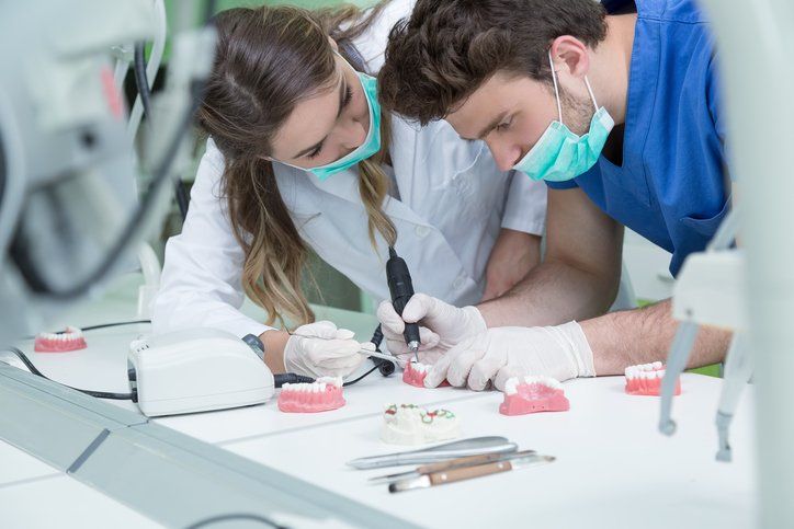 a man and a woman are working on a model of teeth in a dental lab .