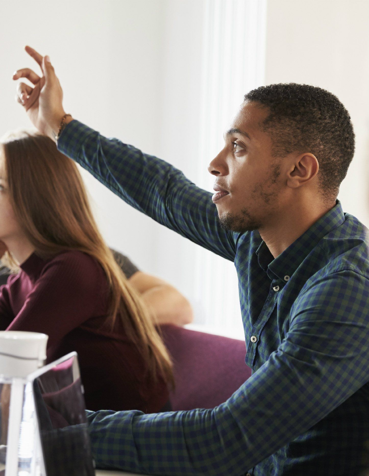 a man in a plaid shirt is raising his hand to answer a question